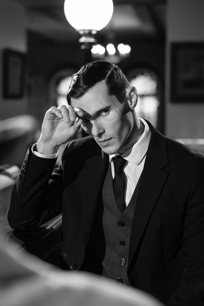 Moody black and white portrait of a man in vintage attire, evoking film noir.